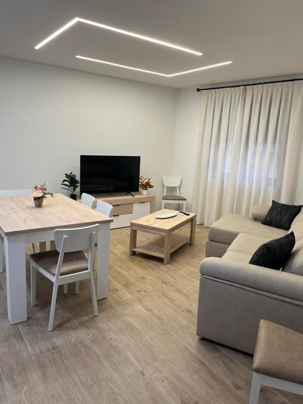 A modern living room with a flat-screen TV, a sofa, a dining table, and a coffee table.