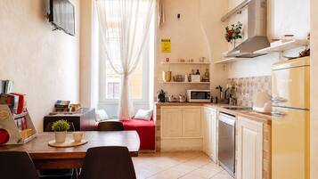 Una cucina compatta con zona pranzo, una TV a muro e una finestra con tende leggere.