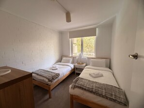 A room with two beds, a wooden nightstand, a bedside table, and a window with a view of greenery. - Newly Renovated Coastal Stay in Mosman Park, 2 Br (Mosman Park)