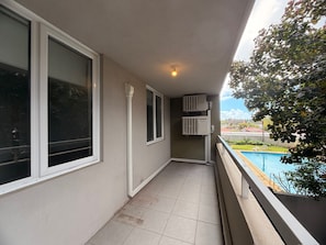 A balcony with a view of a swimming pool, a window, and a wall-mounted air conditioning unit. - Newly Renovated Coastal Stay in Mosman Park, 2 Br (Mosman Park)