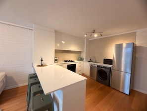 A modern kitchen with white cabinetry, a stainless steel refrigerator, a built-in oven, and a dishwasher. - Newly Renovated Coastal Stay in Mosman Park, 2 Br (Mosman Park)