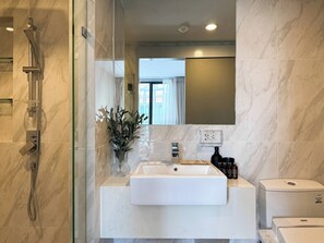 A modern bathroom with a glass-enclosed shower, a white sink, and a mirror above it. - Serene 1-Bedroom Apartment with Pool & Gym in Khlong Toei (Khlong Toei)