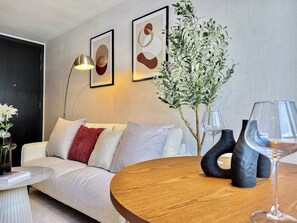 Ein modernes Wohnzimmer mit einer Couch, einem Couchtisch, einer Lampe, einer Vase mit Blumen und einem Weinglas.