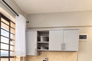 A kitchen with cabinets, a window with curtains, and a wall-mounted electrical outlet. - Likizo Homes - Rehema Apartment, 202, Naivasha (Naivasha)