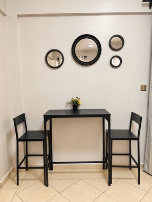 A room with a black table and two chairs, a potted plant on the table, and three wall-mounted mirrors. - Likizo Homes - Rehema Apartment, 202, Naivasha (Naivasha)