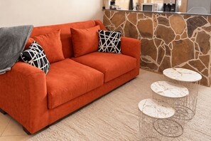 A modern living room with a sofa, patterned cushions, and a stone accent wall. - Likizo Homes - Rehema Apartment, 202, Naivasha (Naivasha)