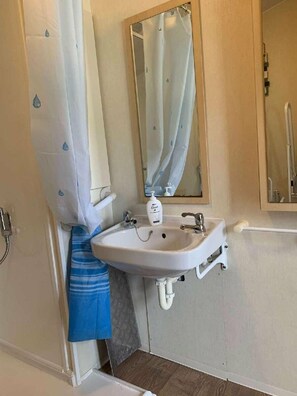 A bathroom with a white sink, a mirror, and a shower curtain. - Lyons Robin Hood - Holiday Accommodation 15838 (Rhyl)