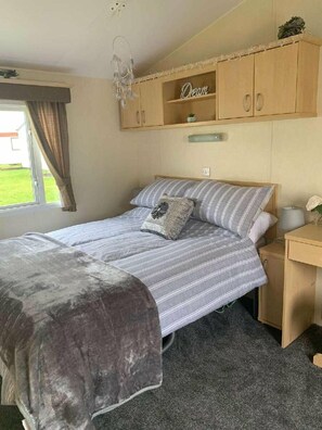 A bedroom with a bed, a bedside table, a nightstand, a wardrobe, and a window with curtains. - Lyons Robin Hood - Holiday Accommodation 15838 (Rhyl)