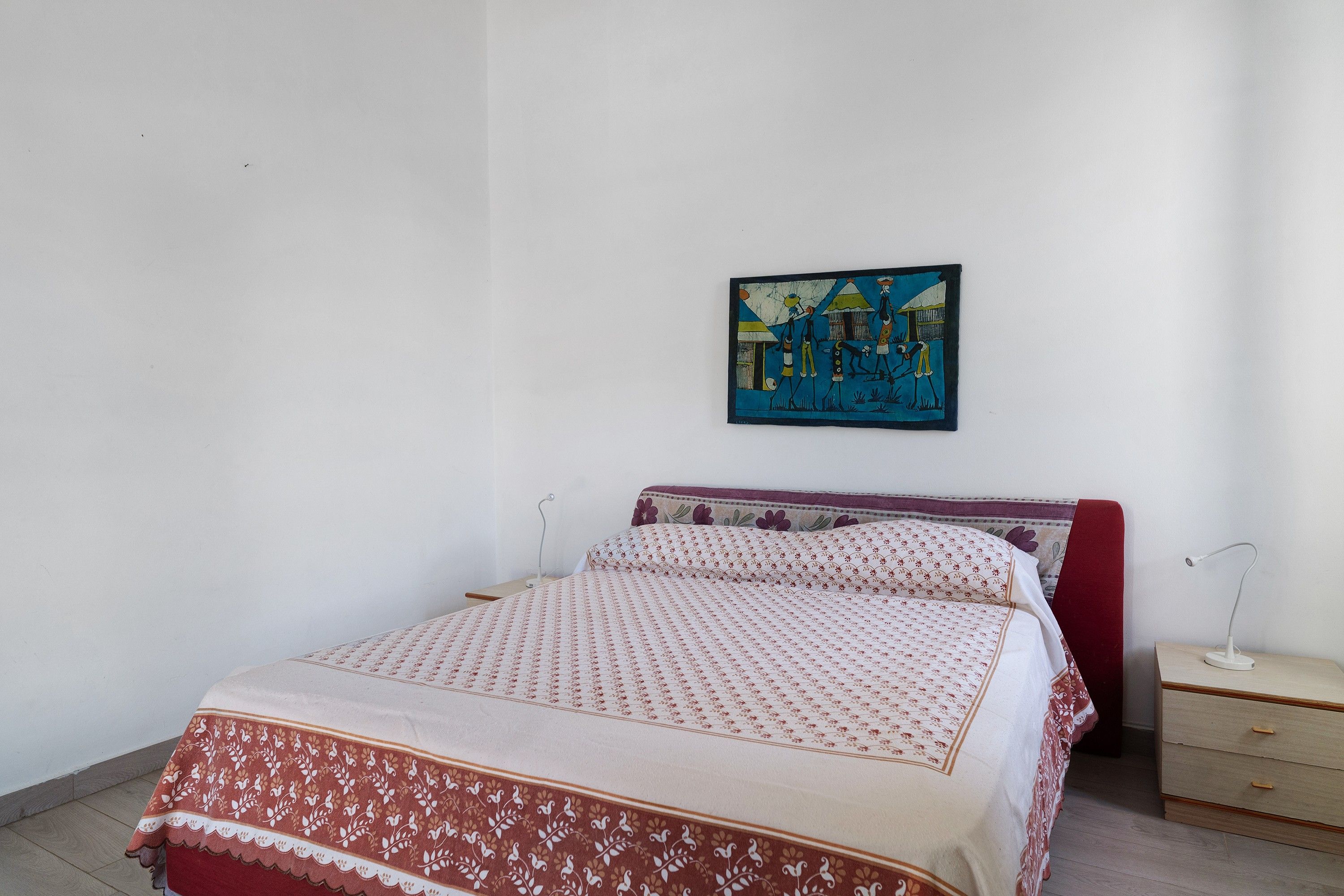 A bedroom with a bed, a nightstand, a lamp, and a wall-mounted painting.