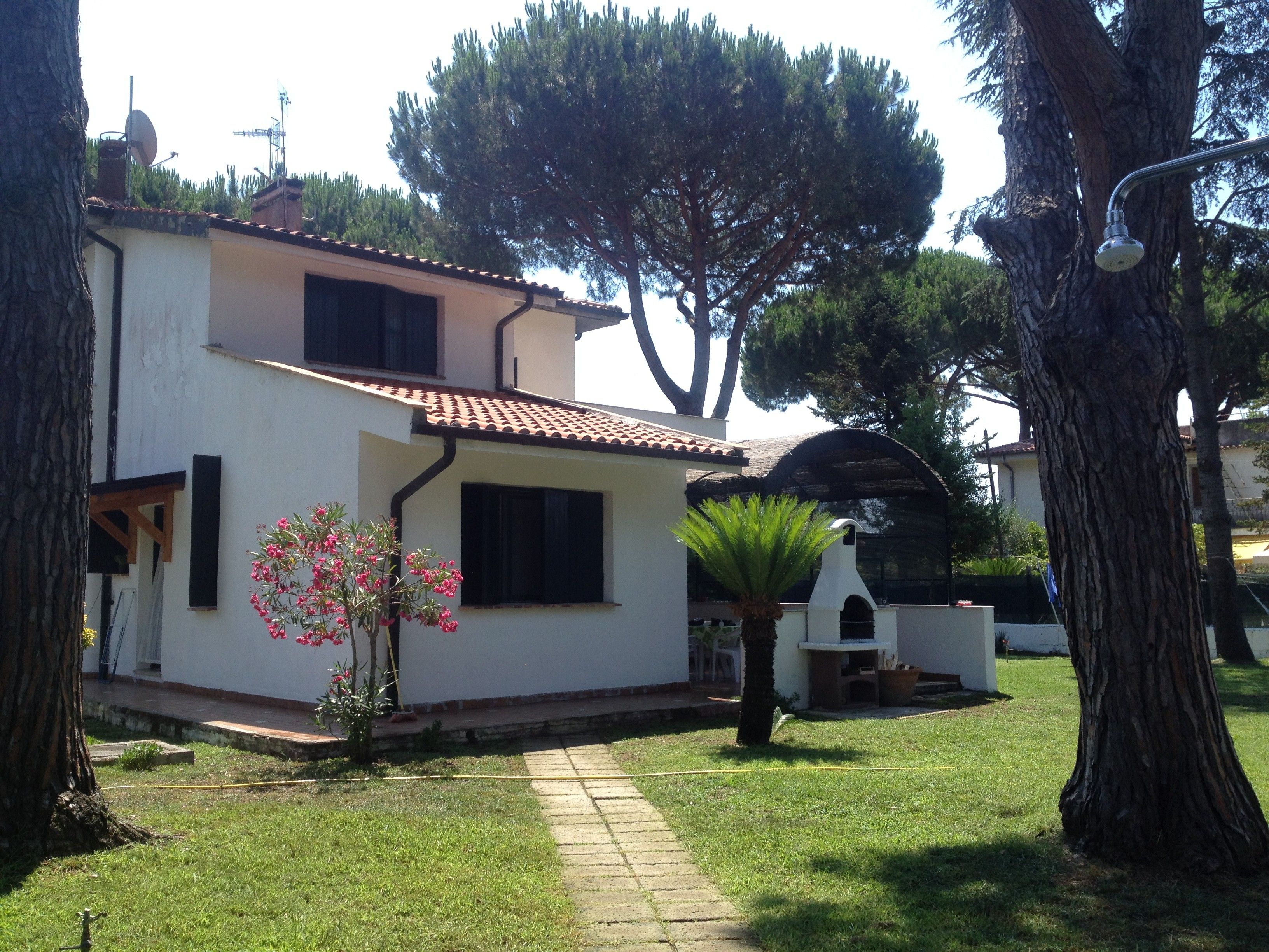 A two-story house with a tiled roof, a small garden with a palm tree, and a satellite dish on the roof.