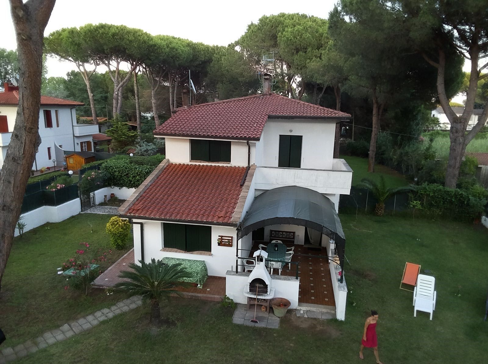 Ein zweistöckiges Haus mit rotem Ziegeldach, einer Terrasse mit Gartenmöbeln und einem kleinen Garten.