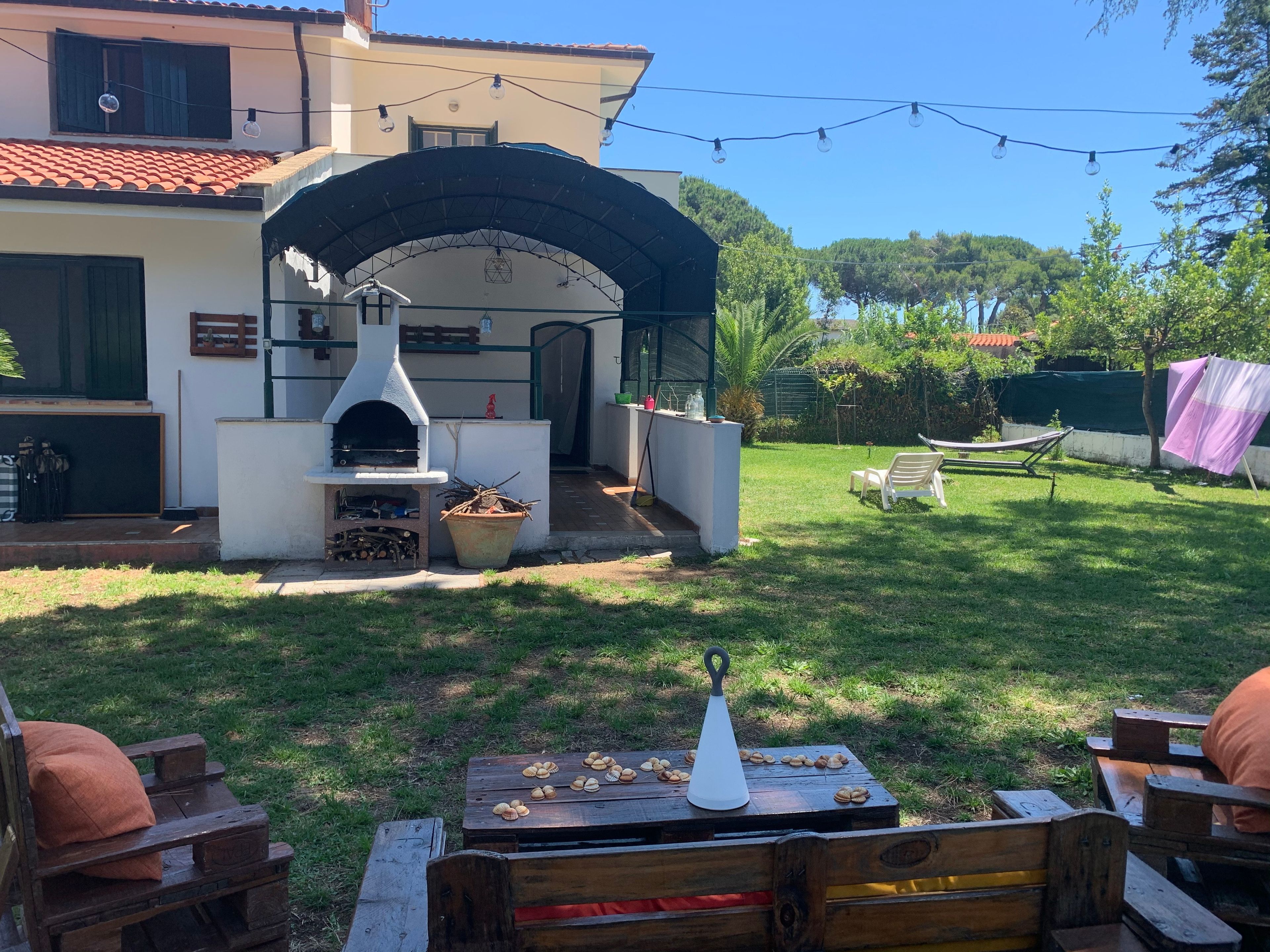 Un giardino attrezzato con forno a mattoni, posti a sedere all'aperto e luci decorative appese.