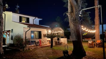 A two-story house with a patio, outdoor lighting, and a tree.