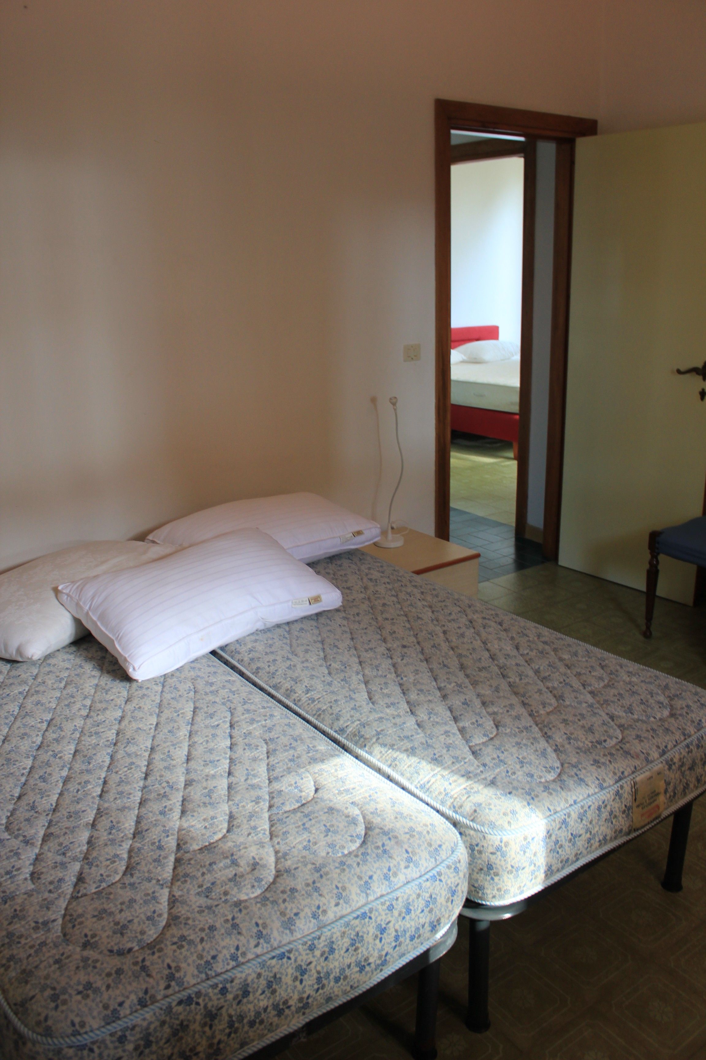 A room with two beds, a wooden nightstand, and a door leading to another room.