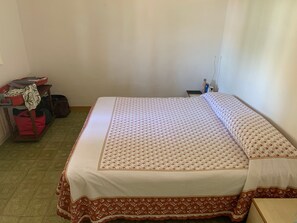 Een kamer met een bed, een klein tafeltje, een stoel en een plank met tassen en een fles.