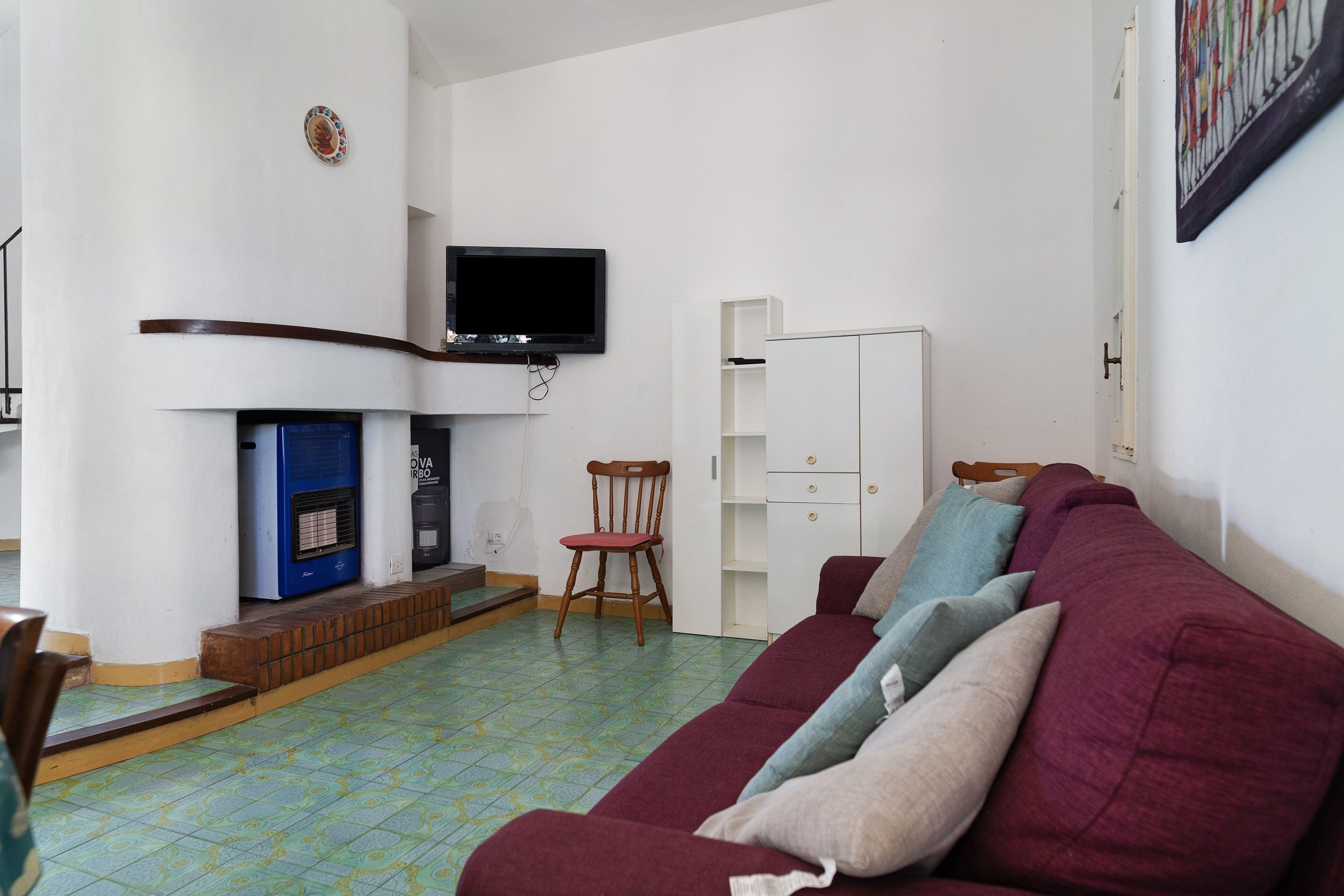 Una sala de estar con un sofá, una televisión sobre la chimenea, un sillón y un aparador.