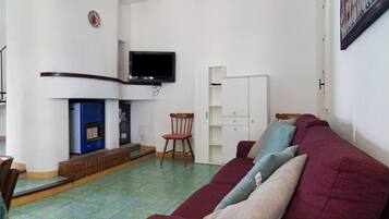 Una sala de estar con un sofá, una televisión sobre la chimenea, un sillón y un aparador.