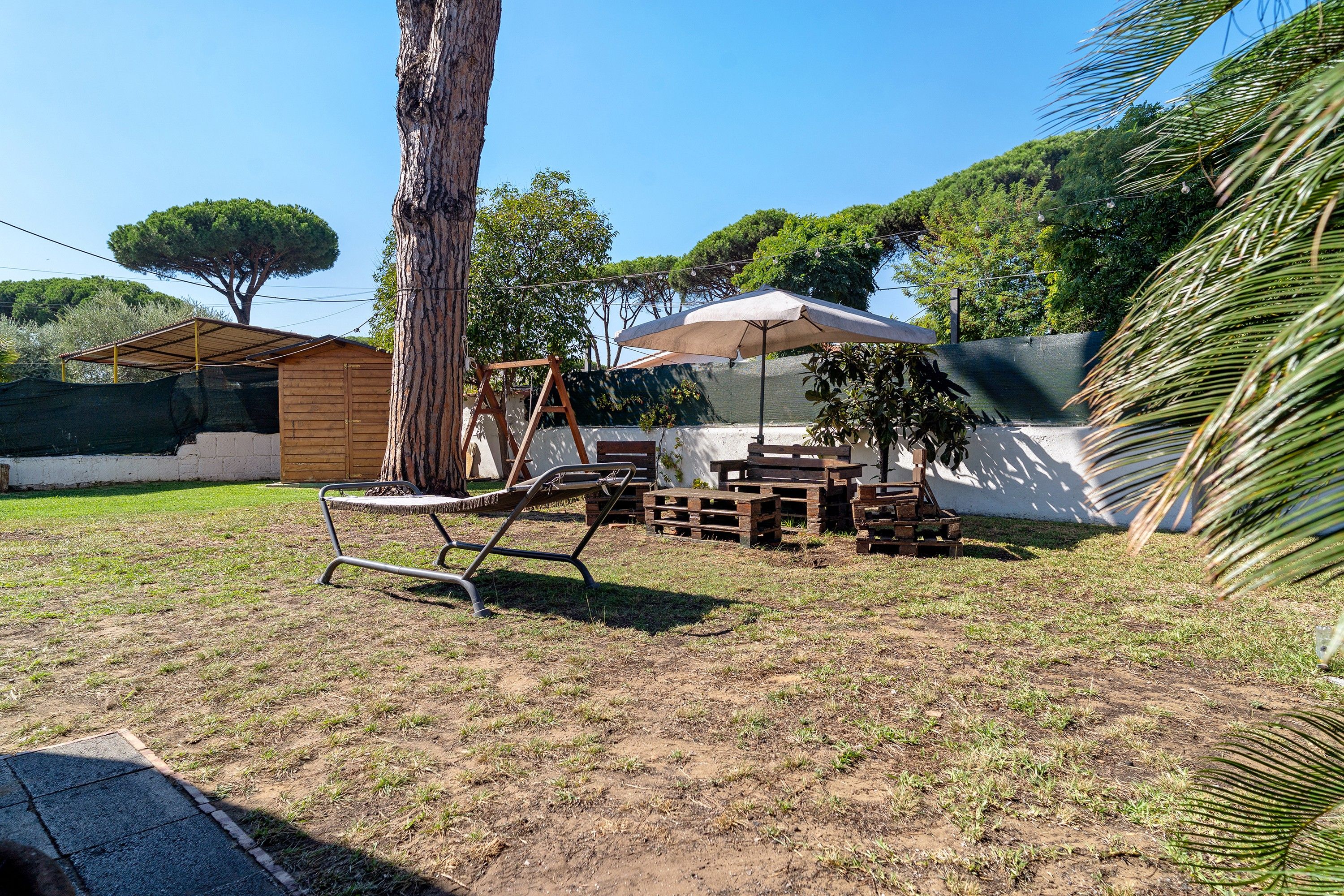 A backyard with a swing set, a wooden table, and a covered seating area.