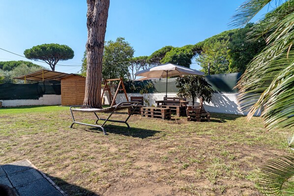 A backyard with a swing set, a wooden table, and a covered seating area.