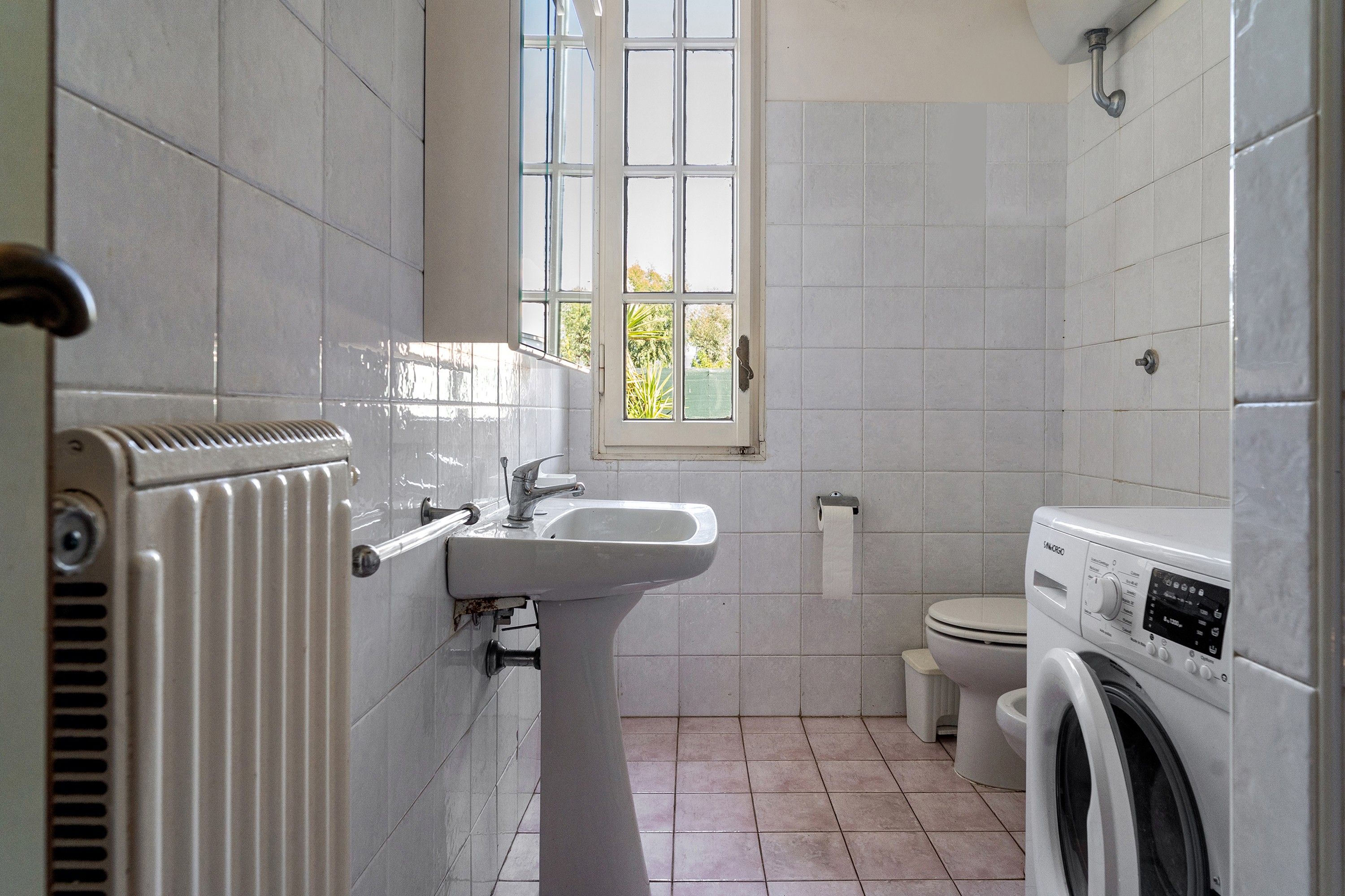 A bathroom with a radiator, a sink, a toilet, and a washing machine.