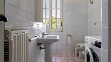 A bathroom with a radiator, a sink, a toilet, and a washing machine.