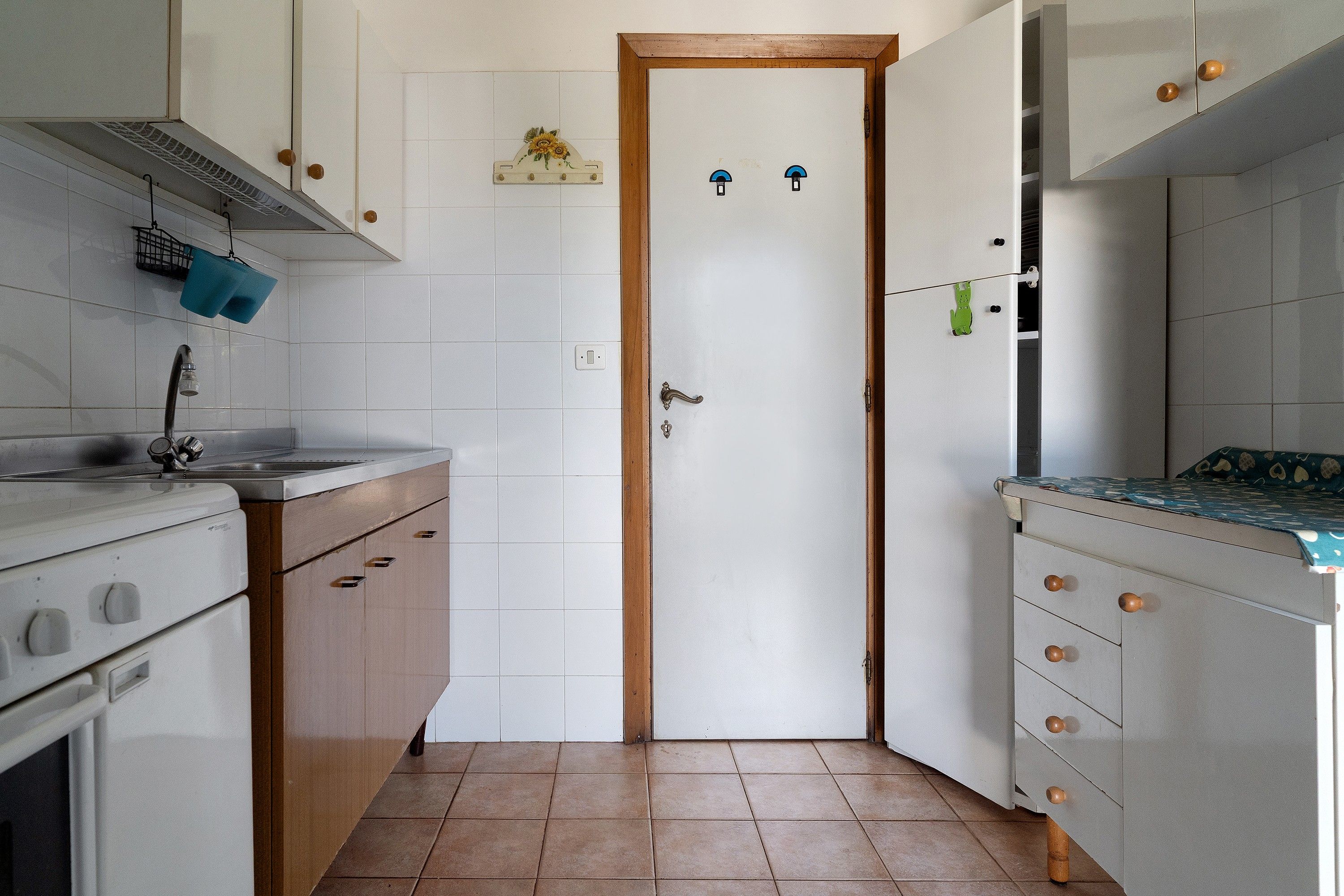A compact kitchen with white cabinets, a wooden door, and a tiled floor.