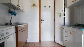 A compact kitchen with white cabinets, a wooden door, and a tiled floor.