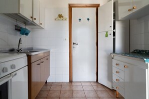 A compact kitchen with white cabinets, a wooden door, and a tiled floor.
