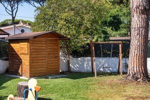 A wooden shed with a sloped roof, a swing set, and a tree in a backyard.