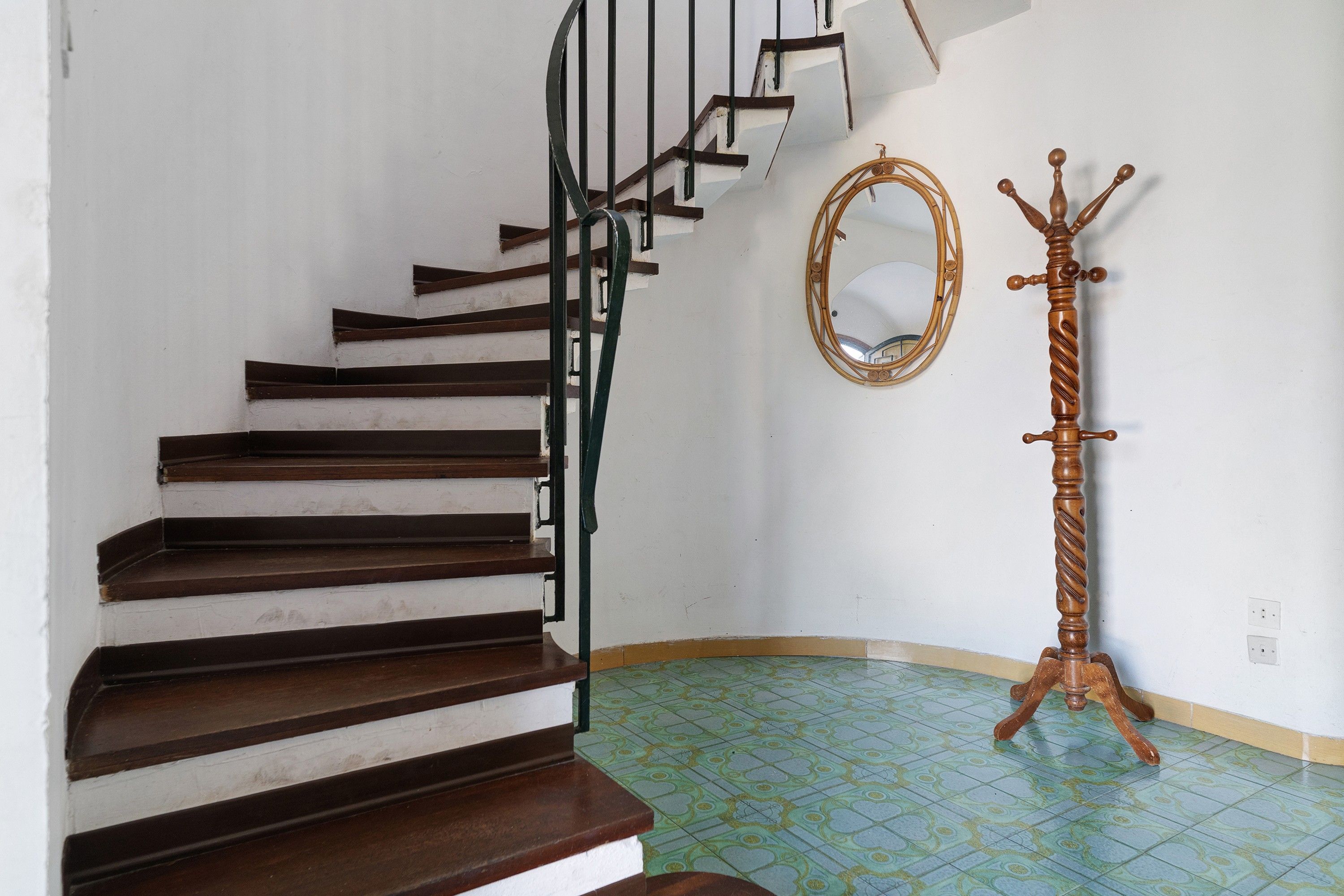Un escalier avec des marches en bois foncé et des rampes en métal noir, un miroir avec un cadre en bois et un porte-manteau en bois.
