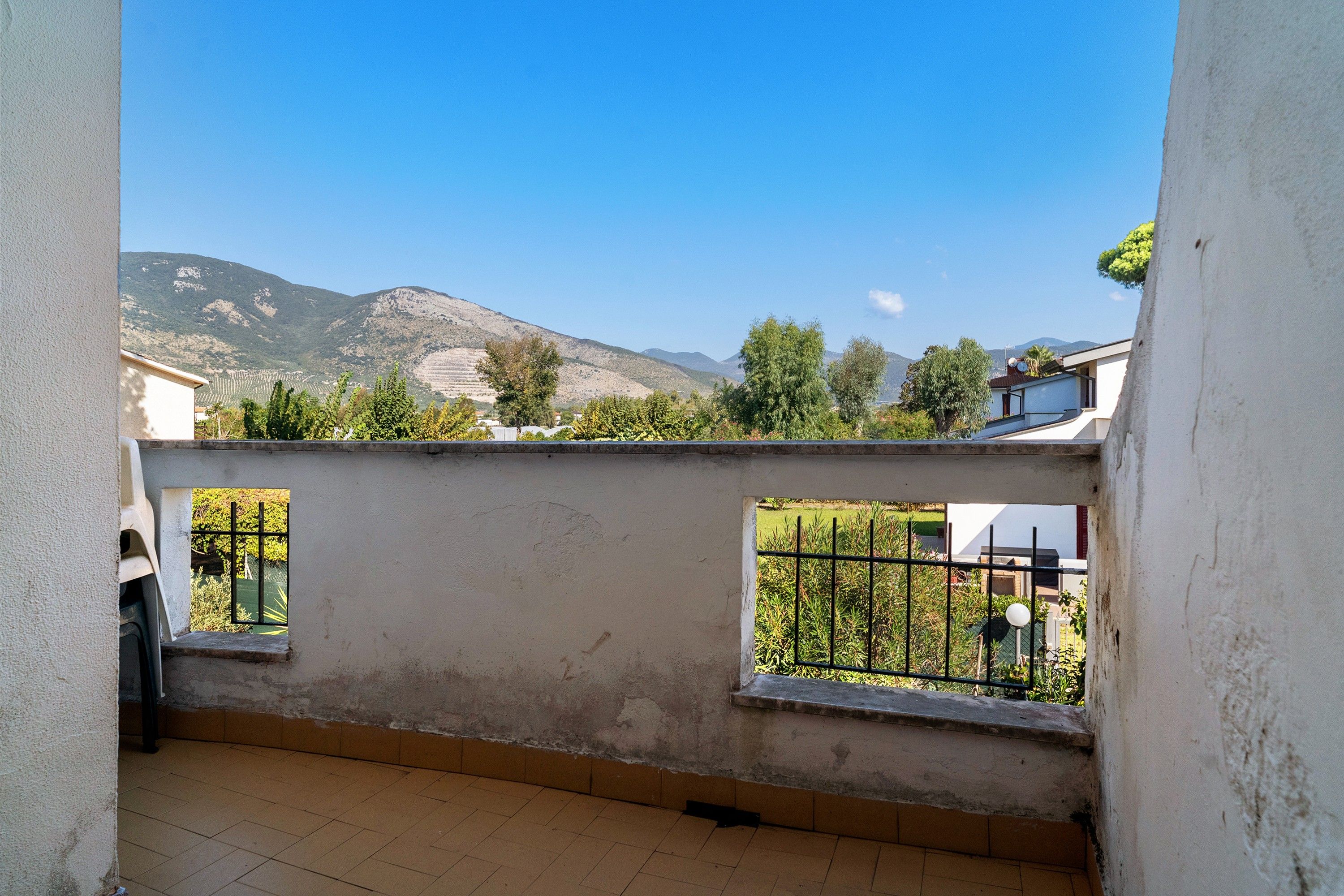 A balcony with a view of a mountain range, a tiled floor, and a white wall.
