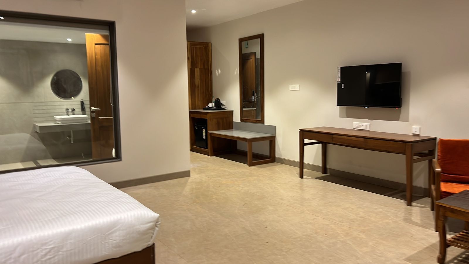 Una habitación de hotel con cama, escritorio, silla, televisor y espejo.