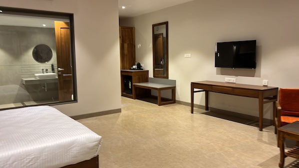 A hotel room with a bed, a desk, a chair, a television, and a mirror. - Reveridge Resort And Spa (Dapoli)