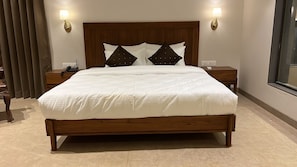 A hotel room with a large bed, wooden headboard, two bedside tables, and wall-mounted lamps. - Reveridge Resort And Spa (Dapoli)