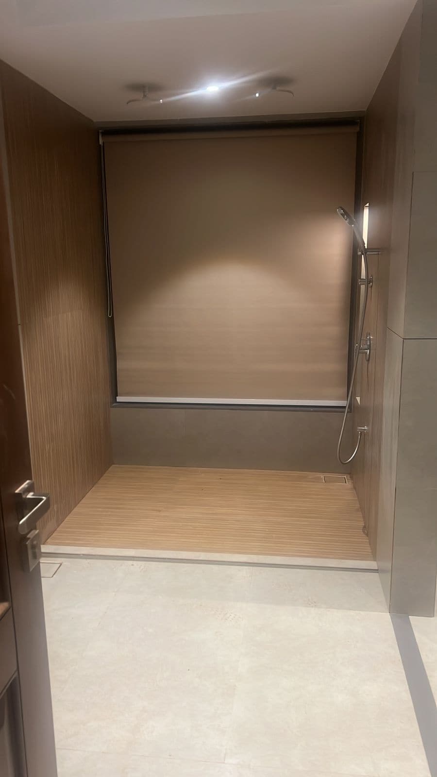 A bathroom with a shower, a wooden door, and a tiled floor.