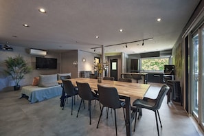 Une cuisine moderne dotée d’un grand îlot central, un coin repas avec une table et des chaises en bois, et un espace de vie avec un canapé et une plante.
