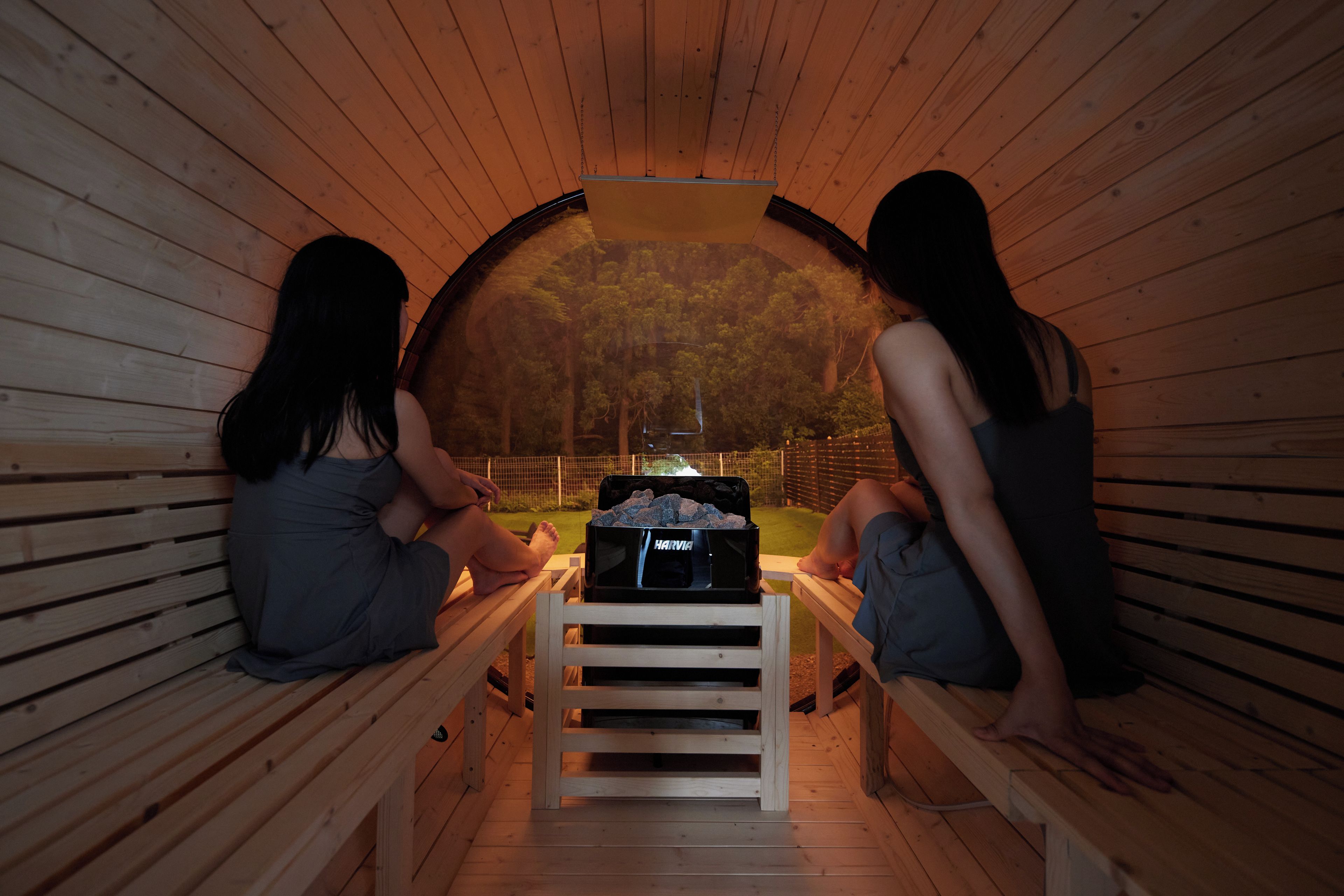 Dos personas sentadas en una sauna con bancos y una mesa central.