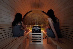 Duas pessoas sentadas em uma sauna com bancos e uma mesa de sauna ao centro.