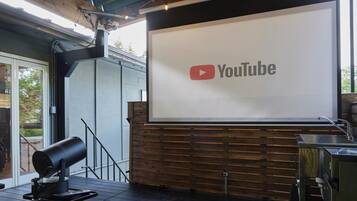 An outdoor area with a large screen displaying the YouTube logo, a projector, and a wooden deck.