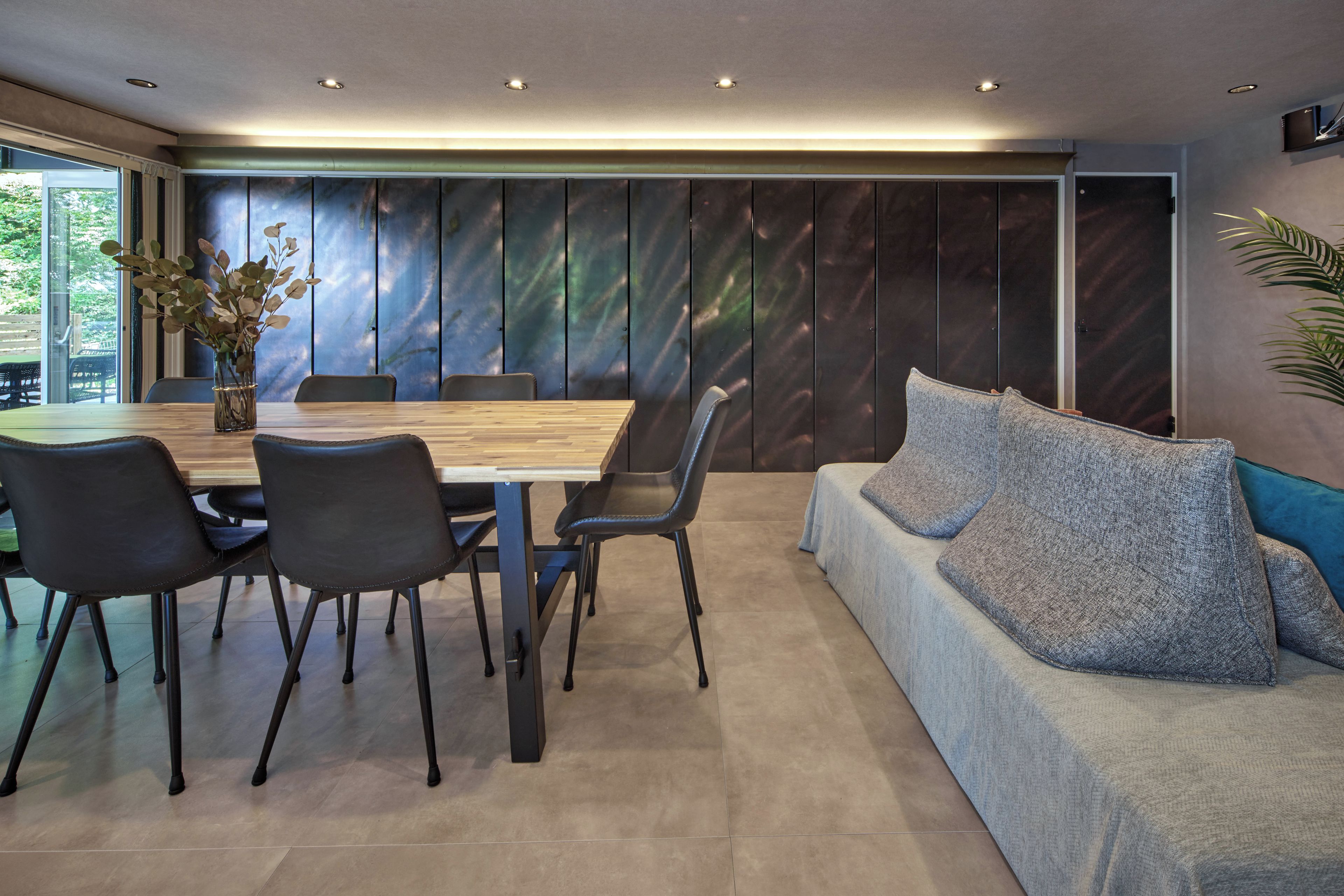 A modern dining area with a wooden table, black chairs, and a blue sofa with grey cushions.