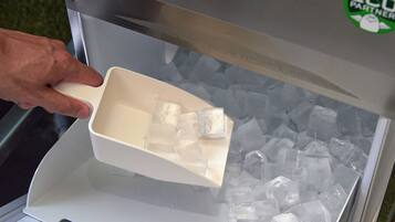 A hand scooping ice cubes from a dispenser.