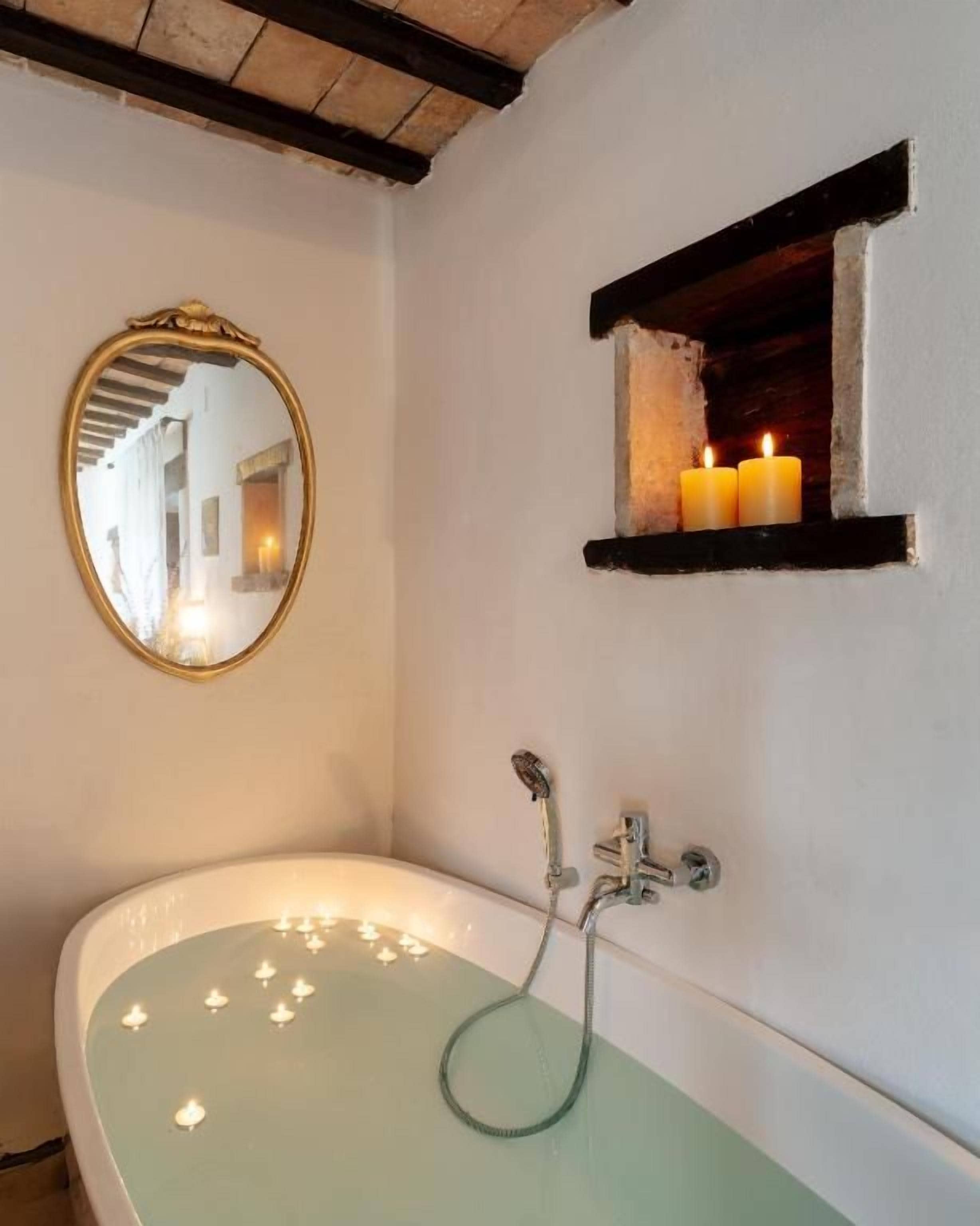 A bathroom with a freestanding bathtub, a mirror, and a shelf with candles.