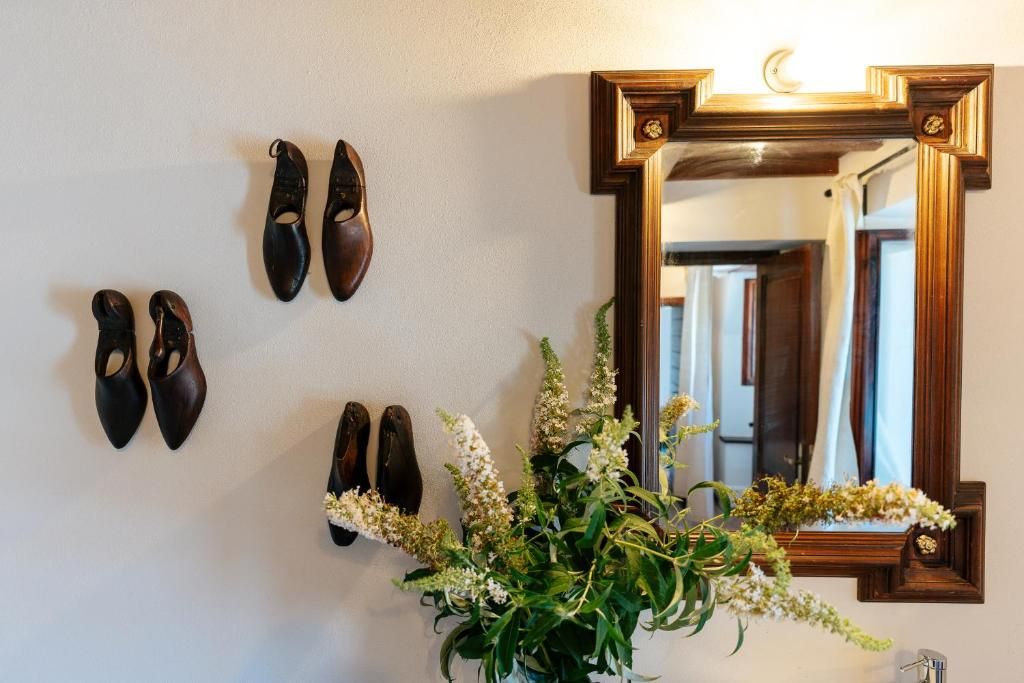 Een wandspiegel met decoratieve lijst, een schoenenrek aan de muur met meerdere paar schoenen, en een potplant met witte bloemen.