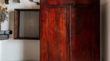 Ein Holzschrank mit einem Metalldrahtgitter dahinter, ein rustikaler Fass und verschiedene Metallplatten an der Wand.