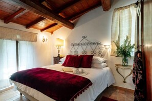 A bedroom with a wooden ceiling, a bed with white bedding and red pillows, a bedside table with a lamp, and a window with curtains. - ROMITO - Relais & Spa (FIUME)