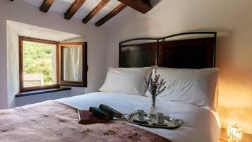 A bedroom with a large bed, a window with curtains, a bedside table with a lamp, and a view of greenery outside.