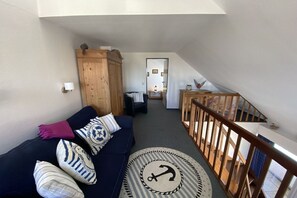 A cozy living area with a dark blue sofa, nautical-themed pillows, a wooden cabinet, and a wooden railing. - Sparrow's Nest Pavilion (Cuxhaven)
