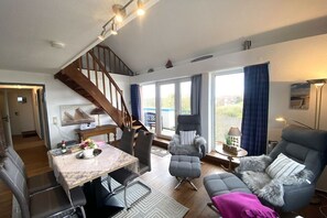 A spacious living area with a dining table, comfortable seating, a staircase, and large windows. - Sparrow's Nest Pavilion (Cuxhaven)
