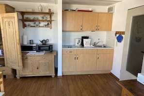 A kitchen with wooden cabinets, a microwave, a kettle, and a coffee maker. - Sparrow's Nest Pavilion (Cuxhaven)