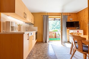 Een keuken met houten kastjes, een eethoek met tafel en stoelen, en uitzicht op een groene buitenruimte.